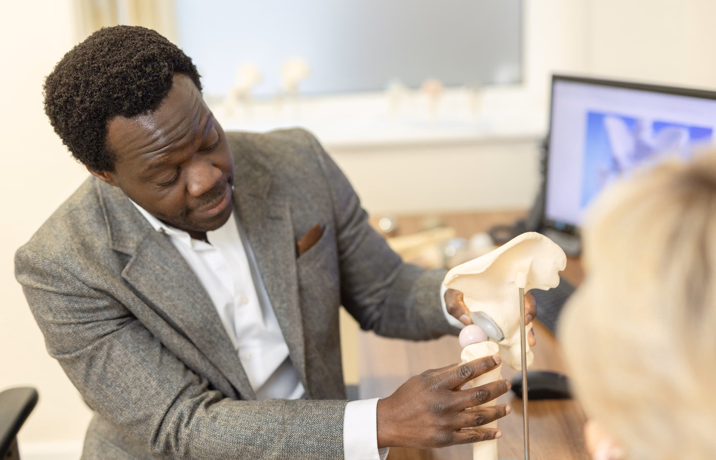 A close up image of Mr Oni showing a female patient a model of an articulating hip joint. The female patient is mainly out of view.
