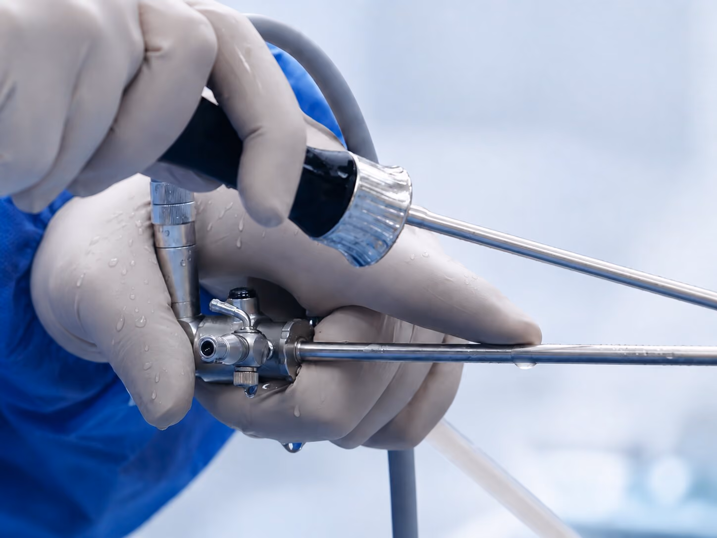 A close up of a doctor performing knee arthroscopy, the hands, handles and first part of the keyhole surgery instrument tools are visible in frame.