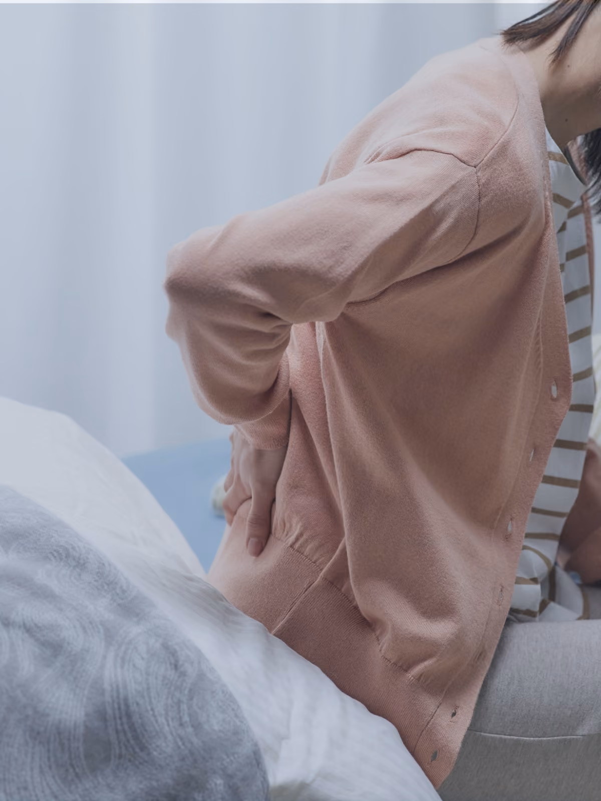 WOman on the edge of the bed holding her painful hip, lower back area.