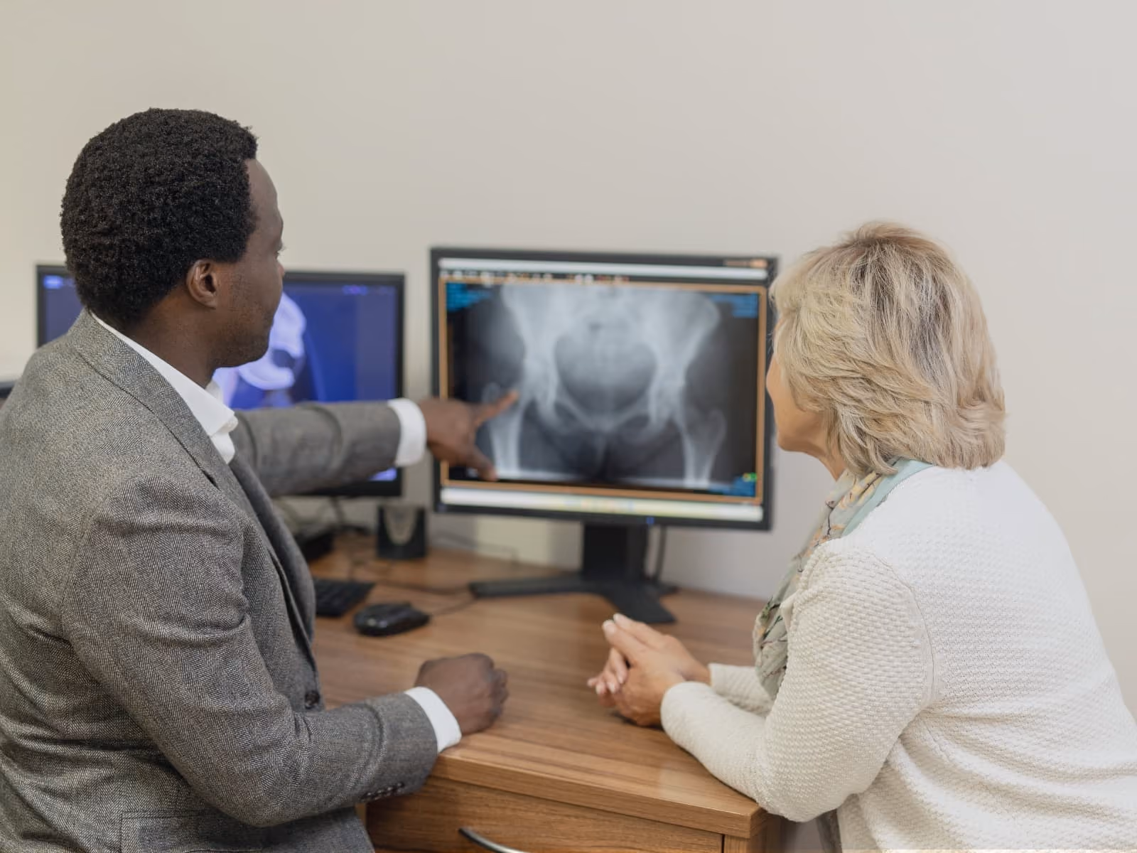 Mr Oni with a female patient, pointing to an x-ray image of her hip joint on his computer screen.