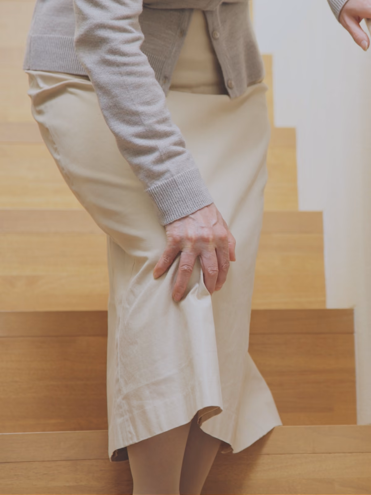 Woman walking down the stairs with a painful knee, she is reaching down girpping her knee