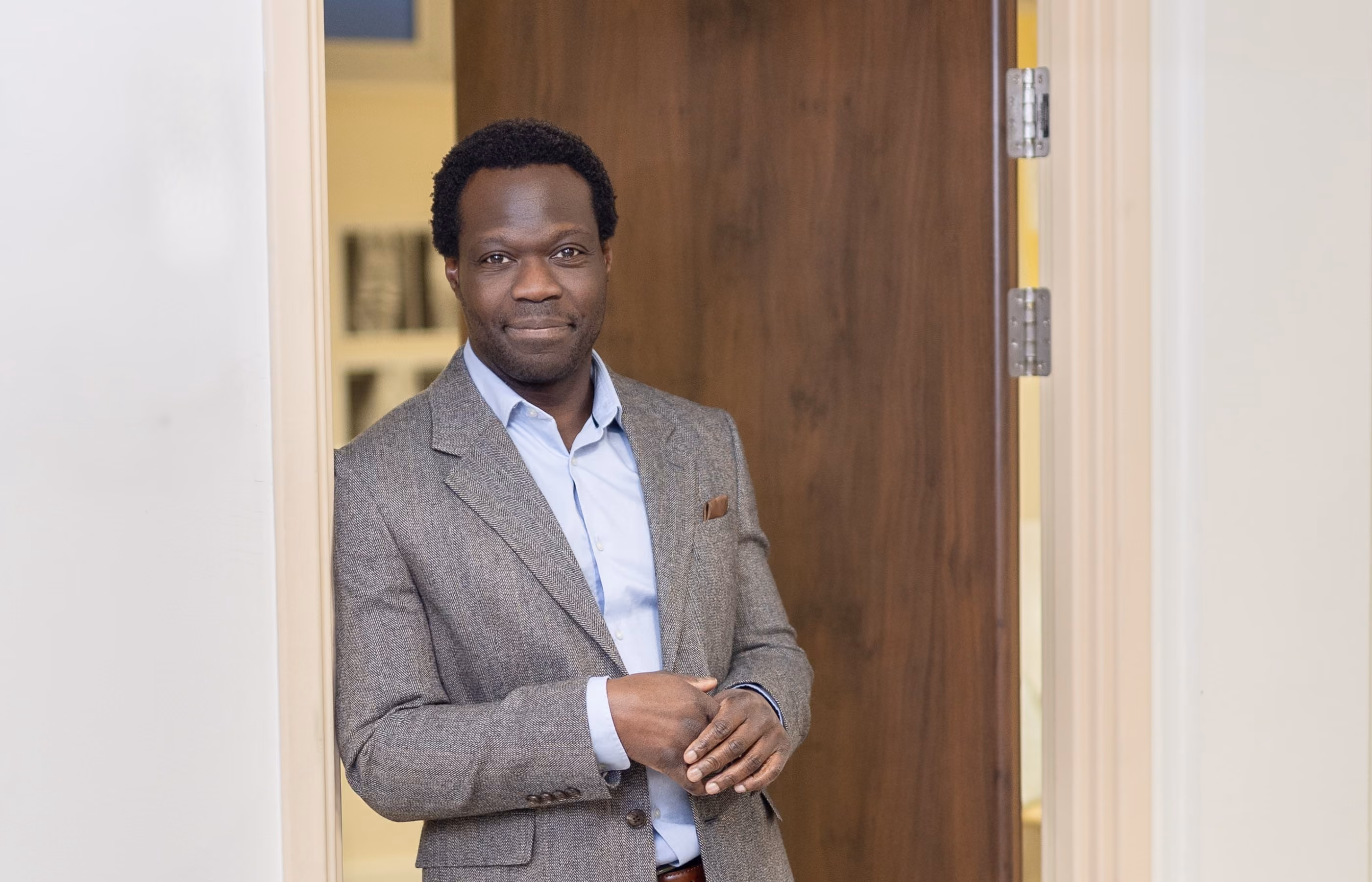 Mr oni in a blazer leaning against his consulting room door frame looking at the camera with a friendly face