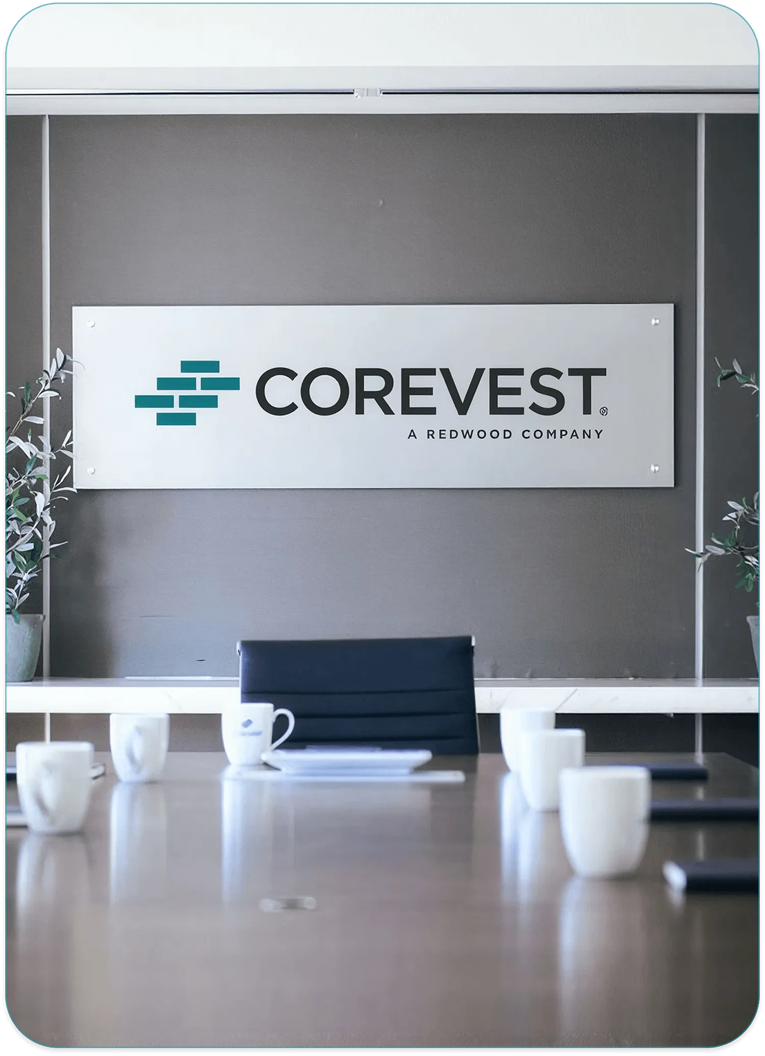 Conference room with a CoreVest, A Redwood Company sign mounted on the wall above a table set with white coffee mugs and a dark office chair.