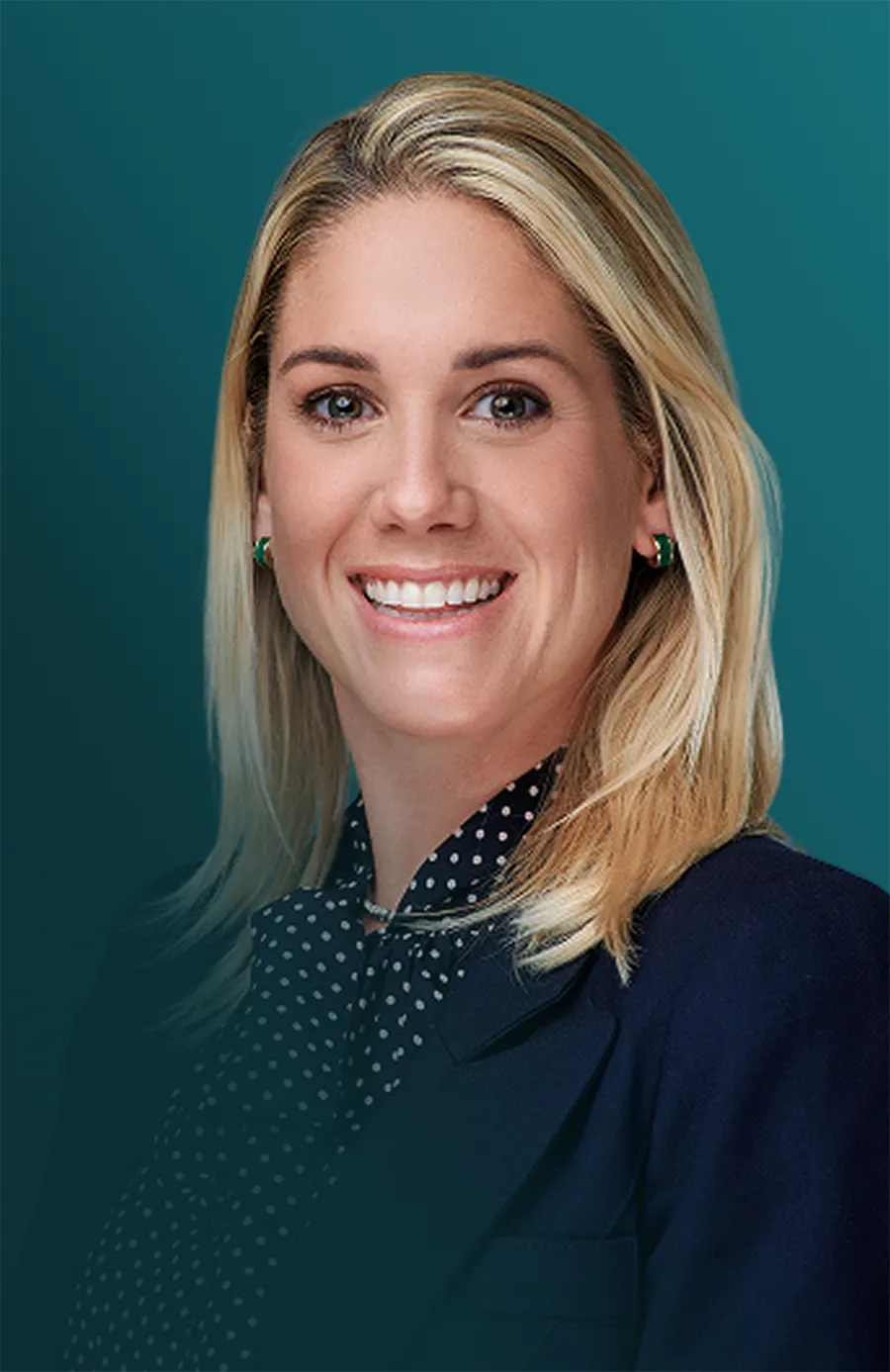 Smiling woman with blonde hair wearing green earrings and a navy blue blazer and polka dot blouse.