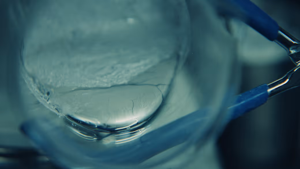 Close-up of a lab tool holding a clear glass container with a translucent gel or liquid inside.