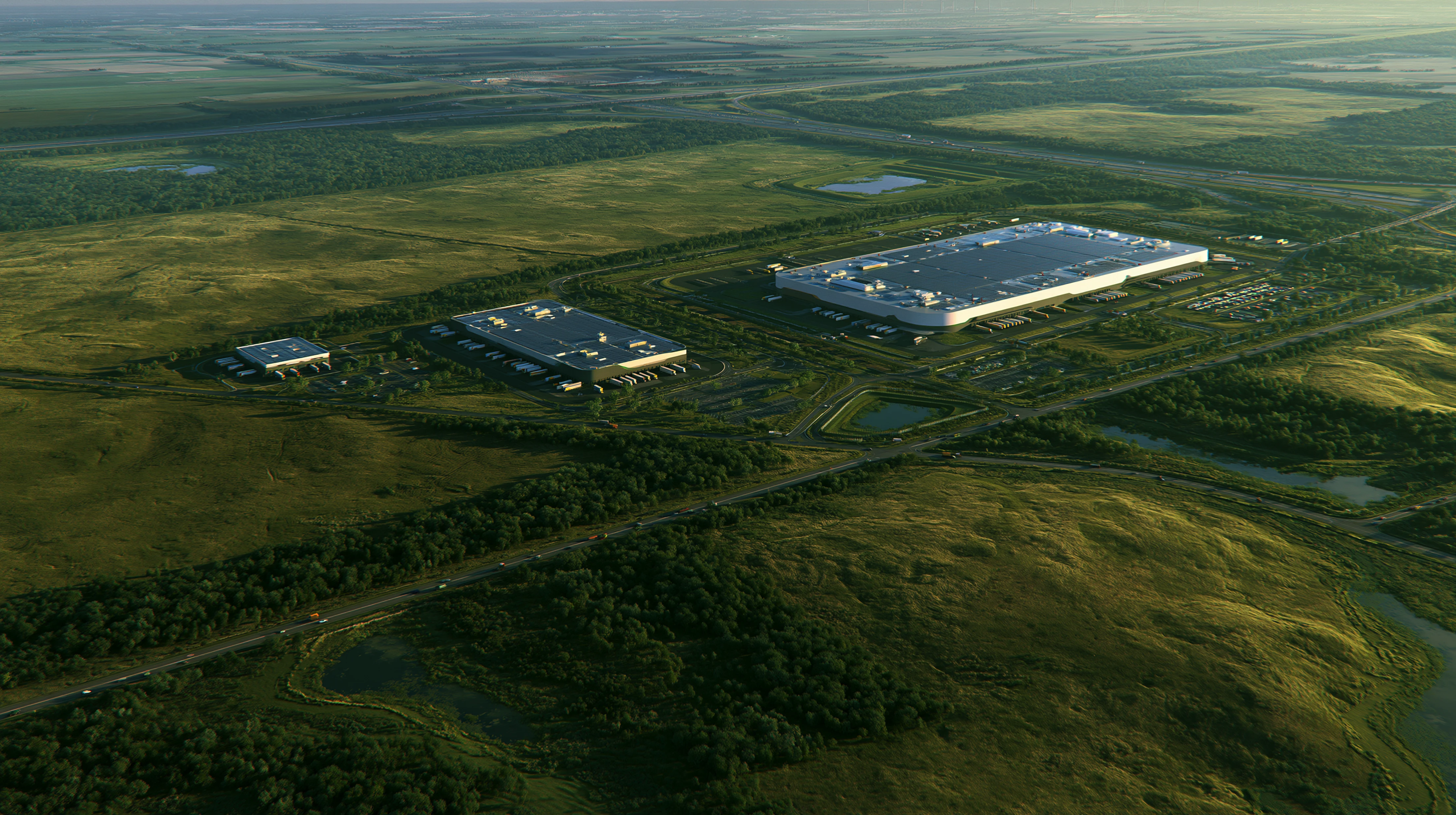 Aerial view of three large warehouse buildings surrounded by green fields and roads.