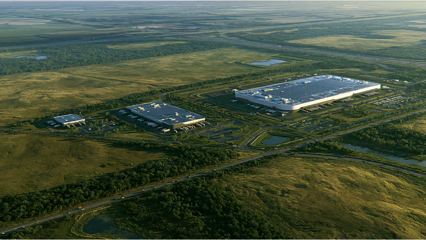Aerial view of three large warehouse buildings surrounded by fields, trees, and roads.