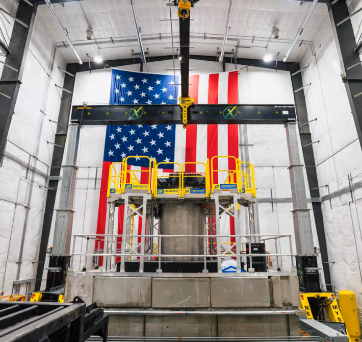 Industrial testing setup with yellow platform in front of a large American flag in a warehouse.