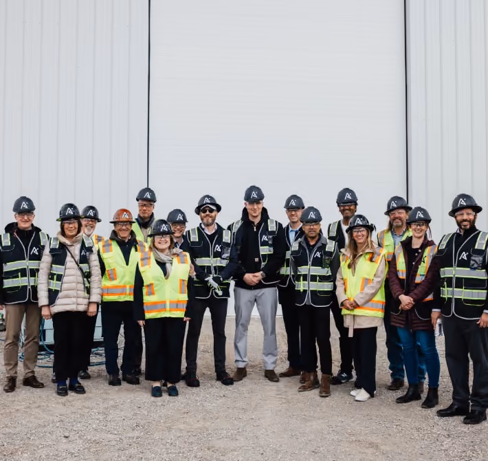 Group of construction workers and staff wearing hard hats and safety vests standing outside a building.