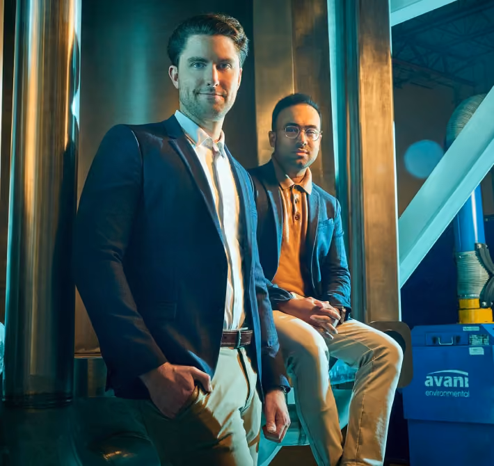 Two men dressed in blazers and light pants posing confidently in an industrial setting.
