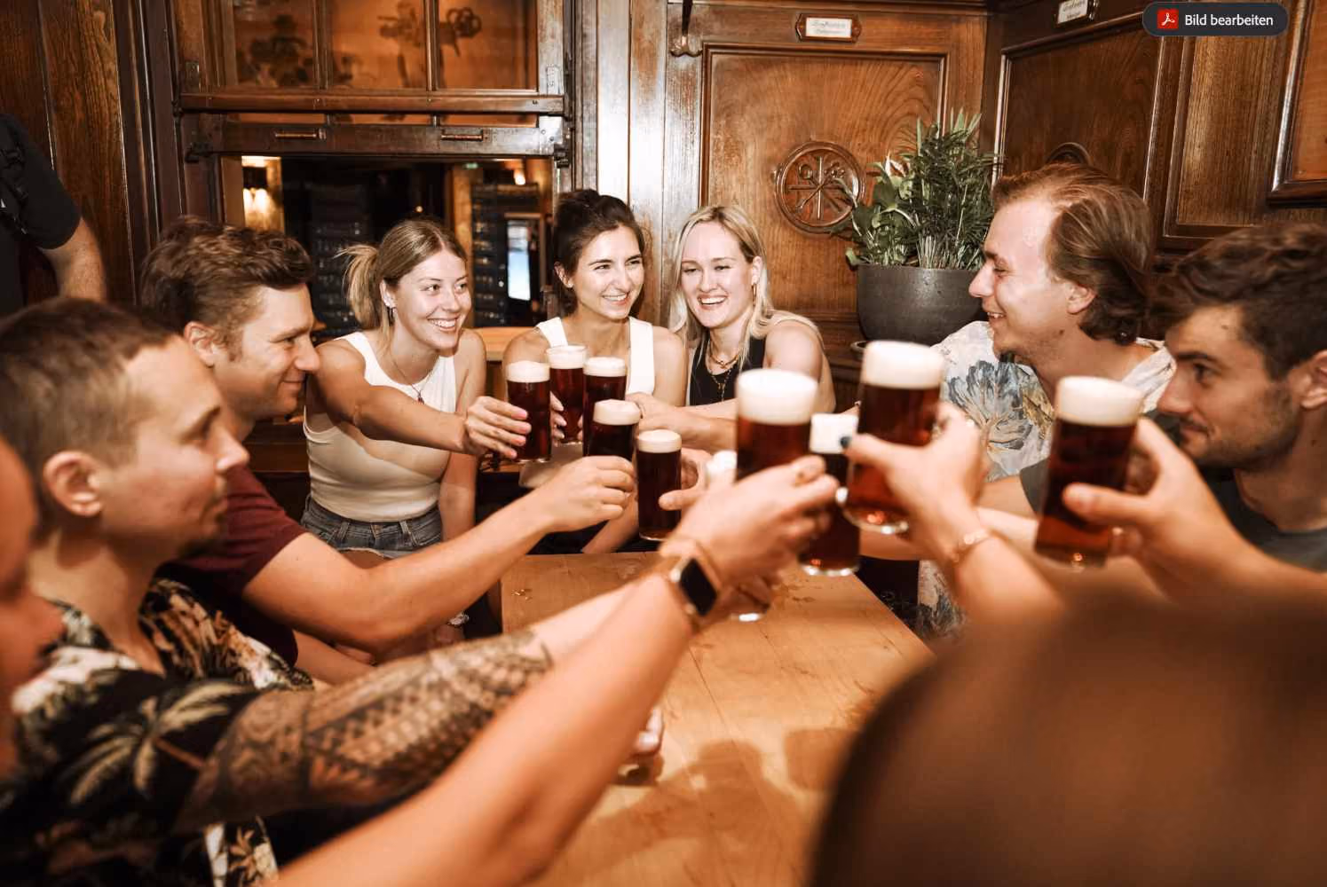 Eine Gruppe von Freunden stößt im stilvollen Gastraum mit Biergläsern an einem Holztisch an.