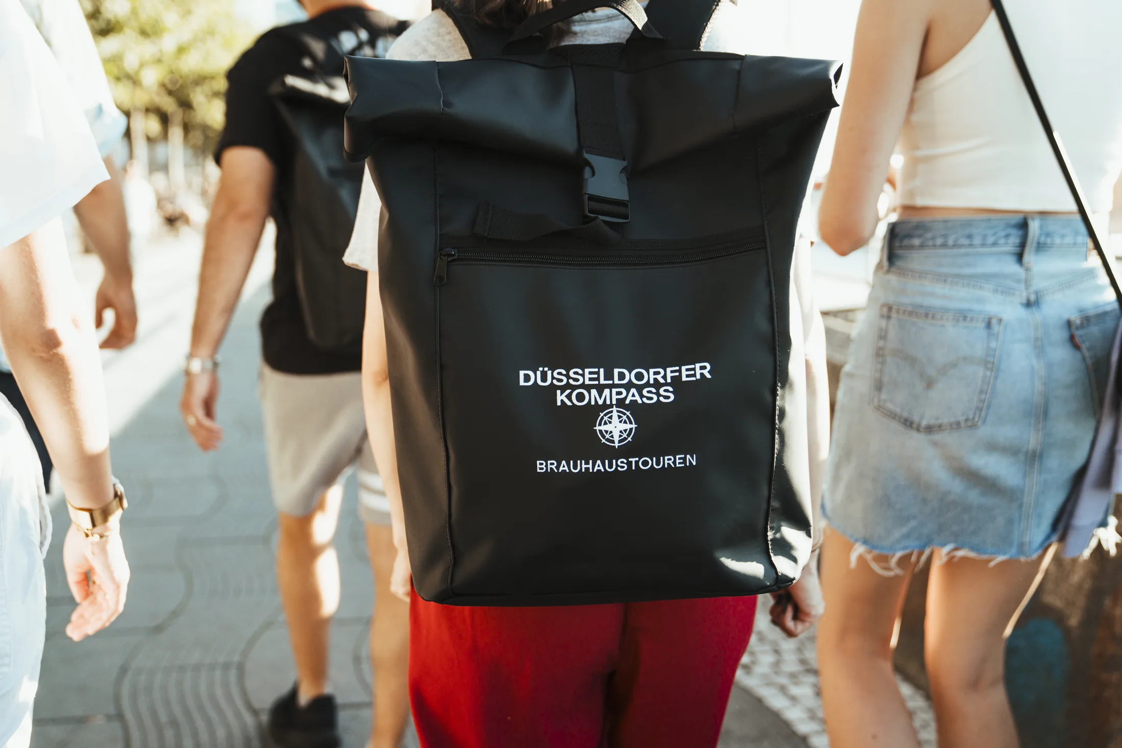 Person trägt schwarzen Rucksack mit Aufschrift Düsseldorf Kompass Brauhaustouren.