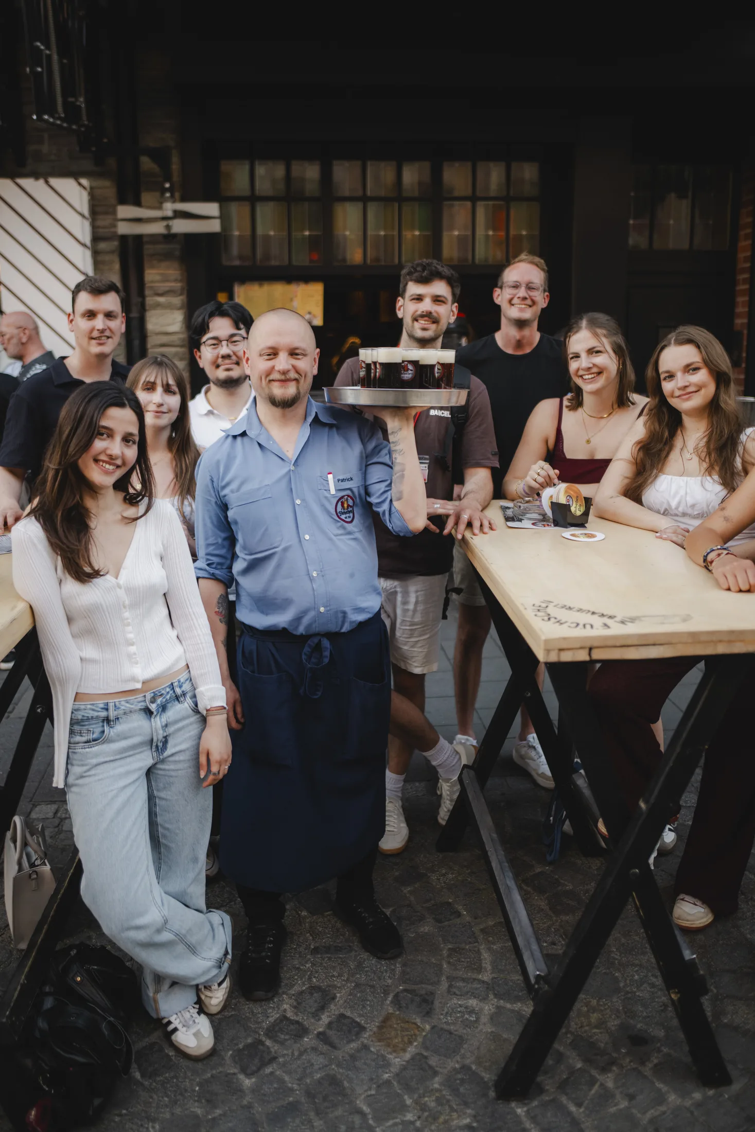 Gruppe junger Leute mit Düsseldorfer Kompass Guide, der ein Tablett mit Biergläsern vor einer Stehtisch Bar hält