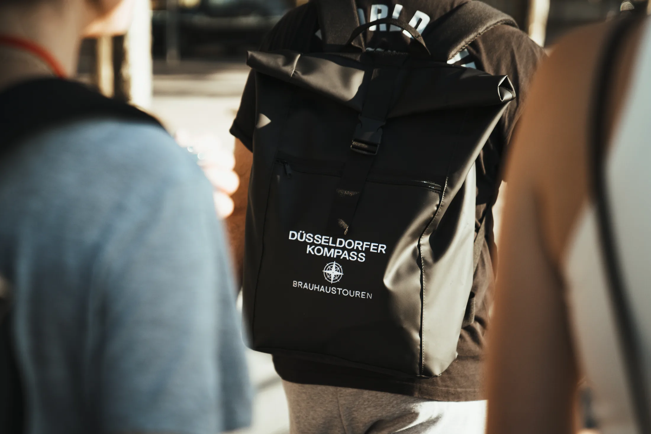 Rucksack mit Aufschrift Düsseldorfer Kompass Brauhaustouren auf dem Rücken einer Person.