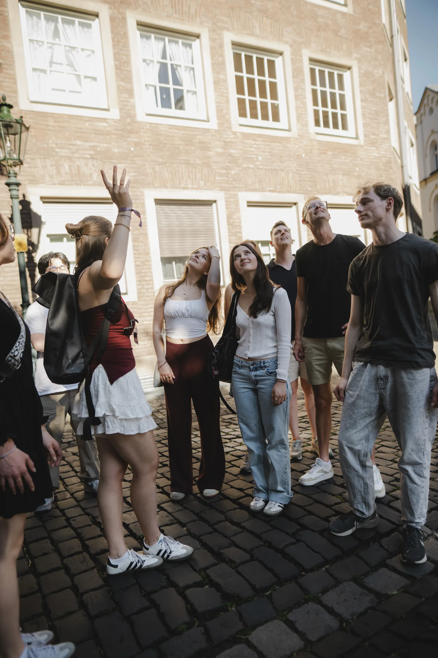 Gruppe junger Menschen auf Kopfsteinpflaster schaut auf einen Stadtführer, der nach oben zeigt.