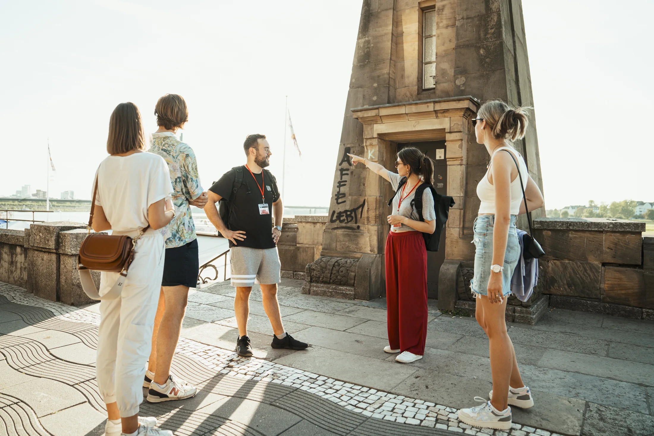 Frau zeigt Gruppe von vier Menschen historische Sehenswürdigkeit an sonnigem Tag im Freien.
