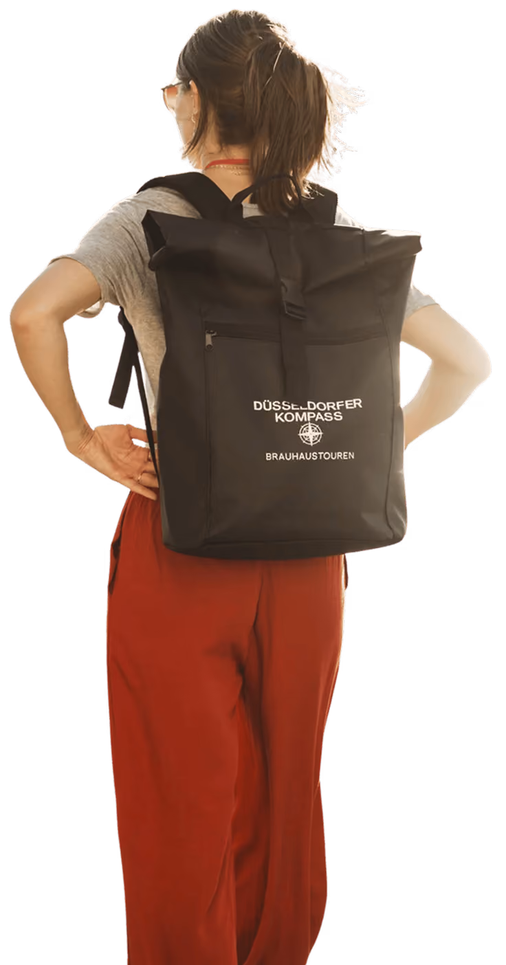 Person mit schwarzem Rucksack mit Aufschrift ‚Düsseldorfer Kompass Brauhaustouren‘ von hinten gesehen.