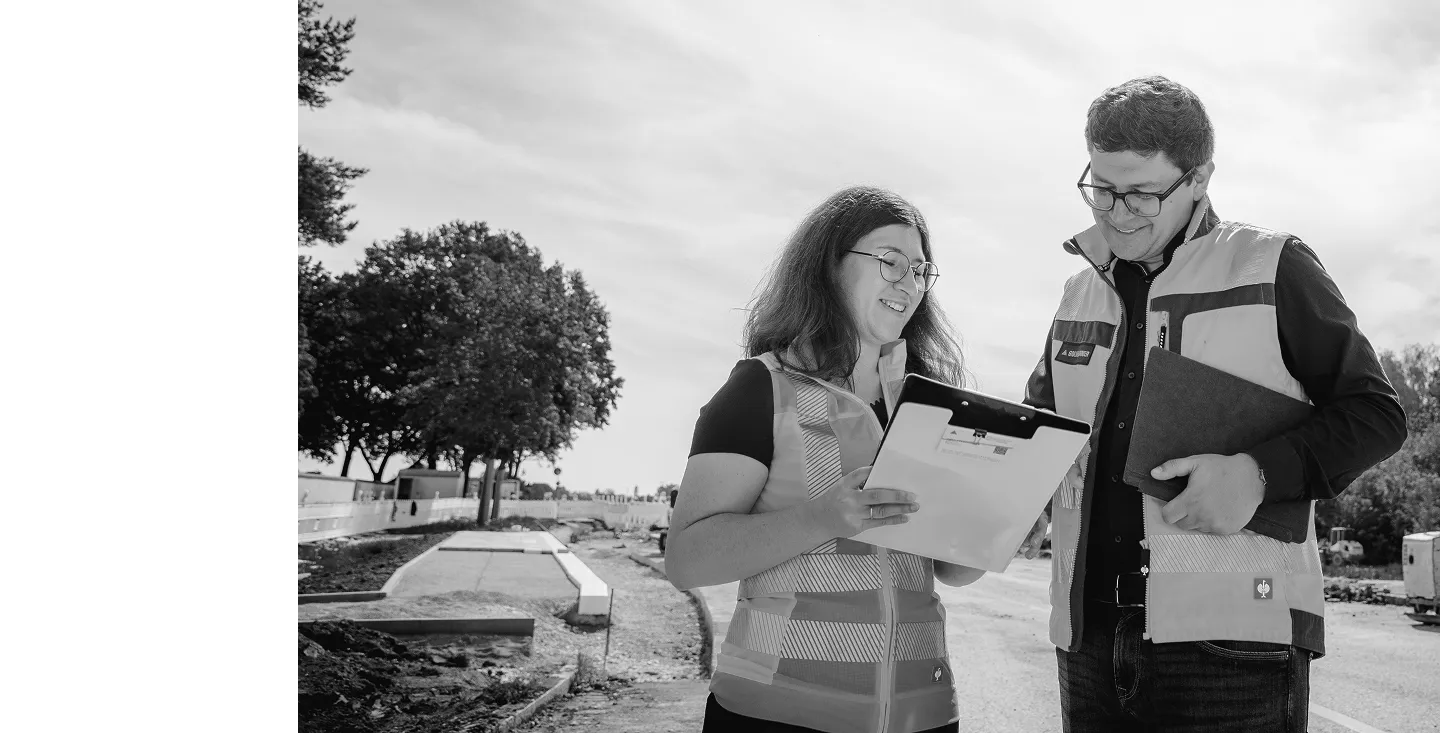 Ingenieurin und Ingenieur in Warnwesten besprechen Pläne auf der Baustelle