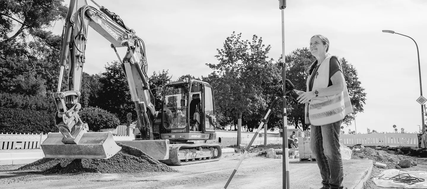Bagger und Mitarbeiter in Warnweste auf einer Straßenbaustelle
