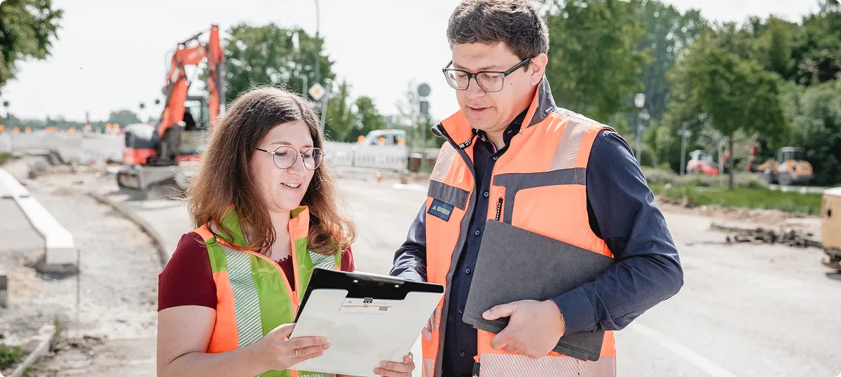 Ingenieurin und Ingenieur mit Unterlagen auf der Baustelle