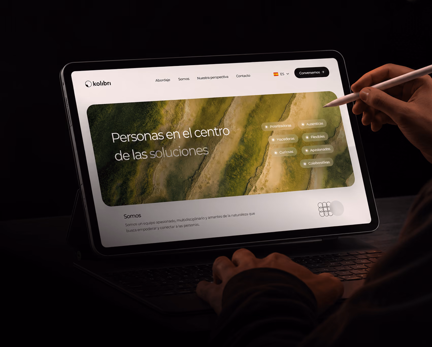 Tablet showing the Kolibri website, with the headline "People at the center of solutions" over an aerial landscape and a hand holding a stylus.