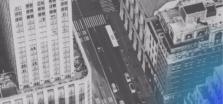 Black-and-white aerial view of a city street between tall buildings, with a blue gradient in the corner.