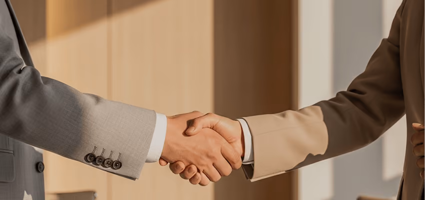 Close-up of two people in suits shaking hands in a warmly lit office.