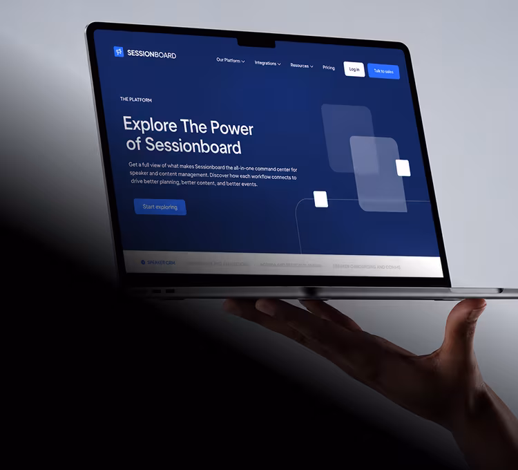 Hand balancing a MacBook showing the Sessionboard website hero "Explore The Power of Sessionboard" on a dark blue layout
