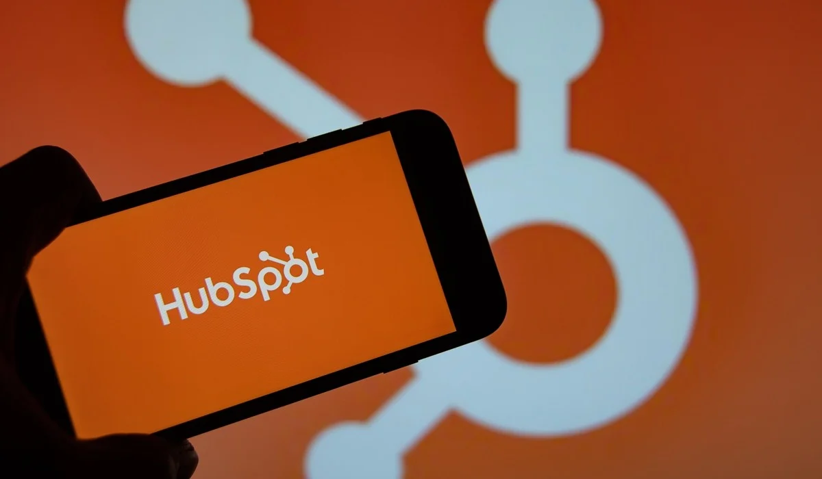 Personne utilisant un smartphone affichant l'écran orange avec le logo HubSpot au centre.