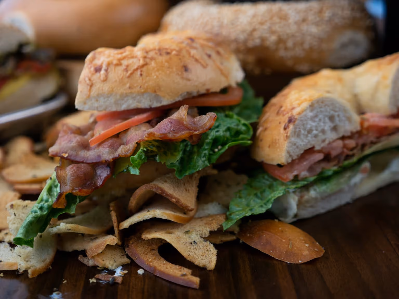 Bacon, lettuce, and tomato sandwiches on toasted buns with potato chips on a wooden surface.