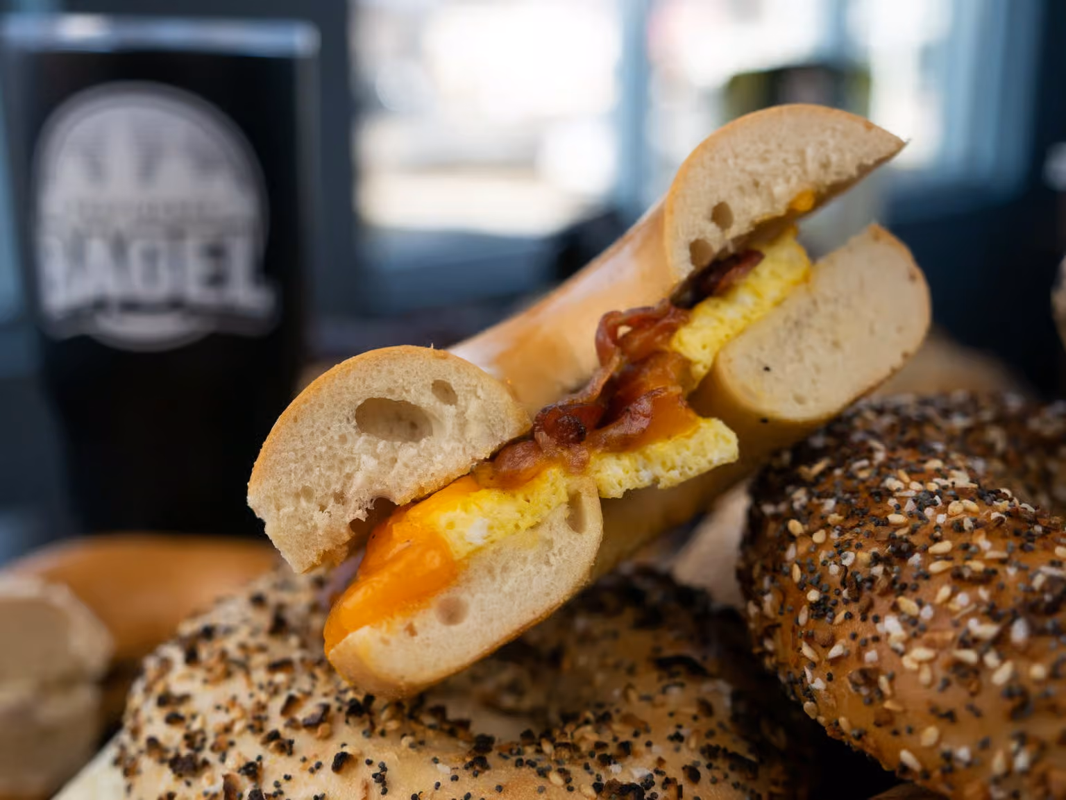 Bagel sandwich with scrambled egg, bacon, and cheddar cheese on top of seasoned bagels.