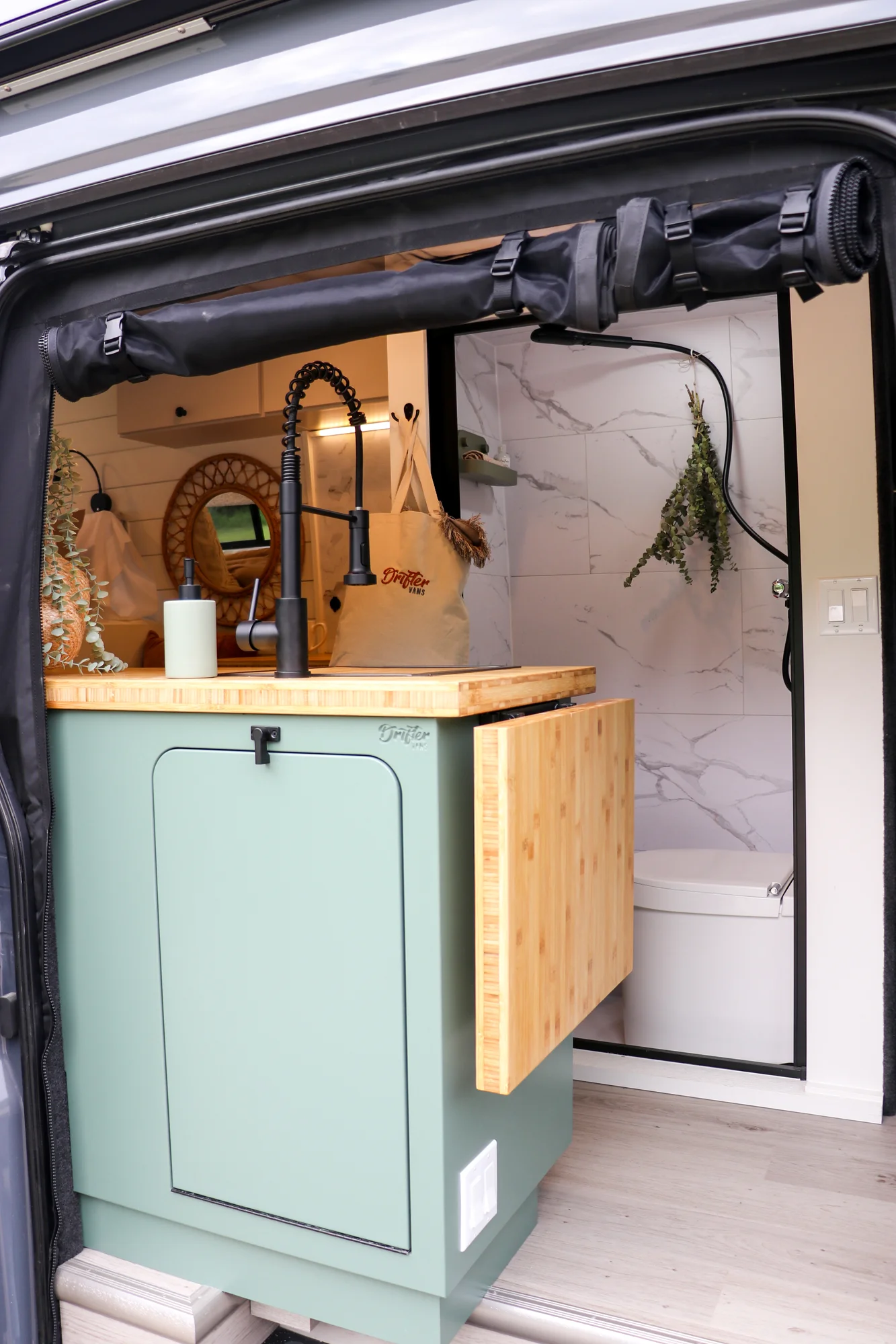 The Drifter 101 custom Ford Transit campervan built for Mallory and Matt by Drifter Vans, Nomadik layout with a bamboo countertop, matte black fixtures, marble shower, and Abyss Grey exterior
