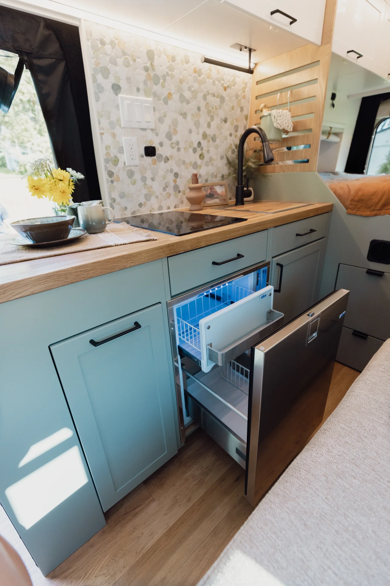 The Drifter 101 custom Ford Transit campervan built for Judy by Drifter Vans, Drifter layout with a boho interior, white oak butcher block, Honey Onix tile backsplash, and Avalanche Grey exterior