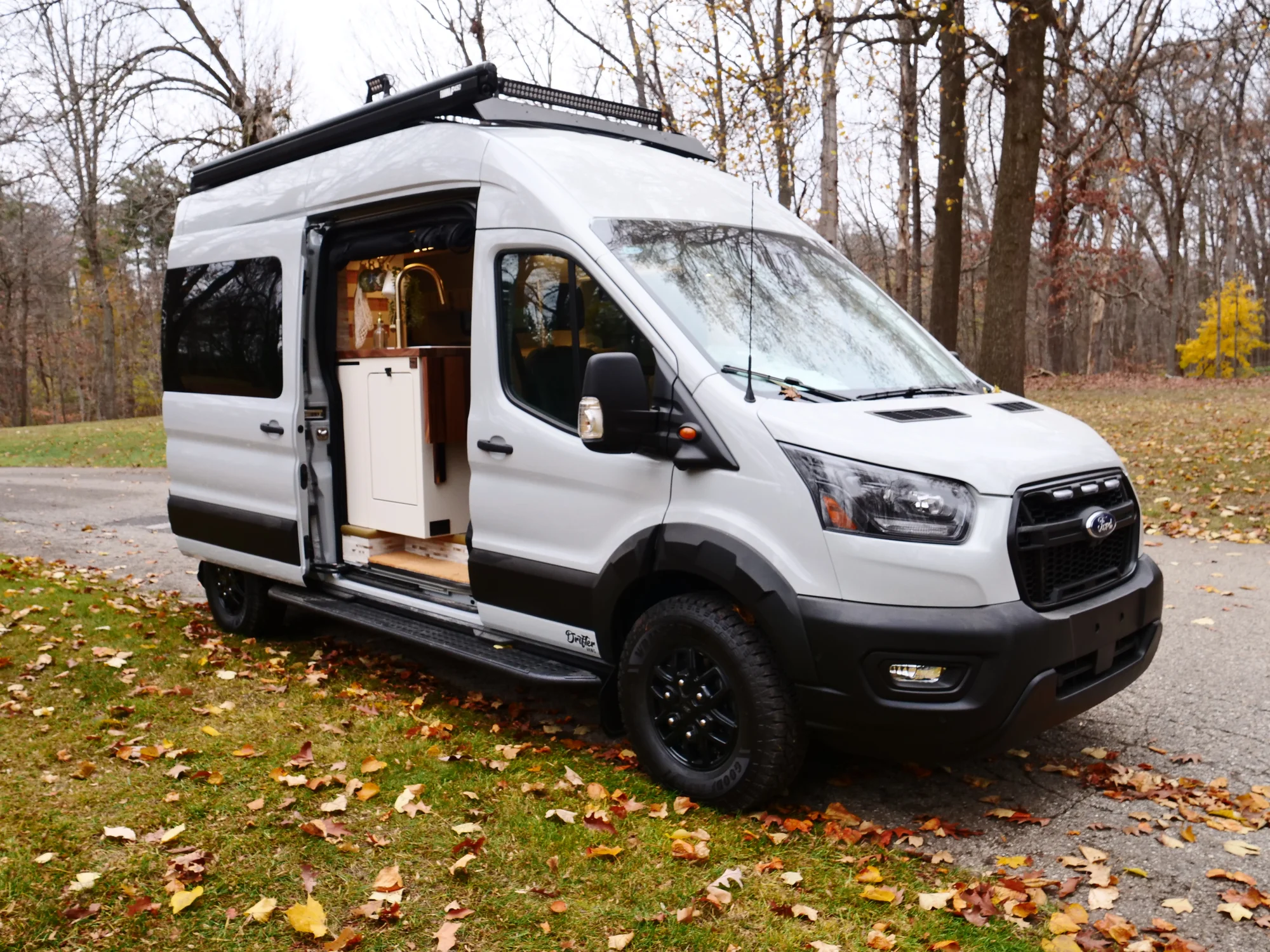 The Drifter 101 custom Ford Transit campervan built for Lori by Drifter Vans, Wanderer layout with a modern farmhouse interior, maple butcher block countertop, gold fixtures, and an exterior FVCO roof rack and ladder