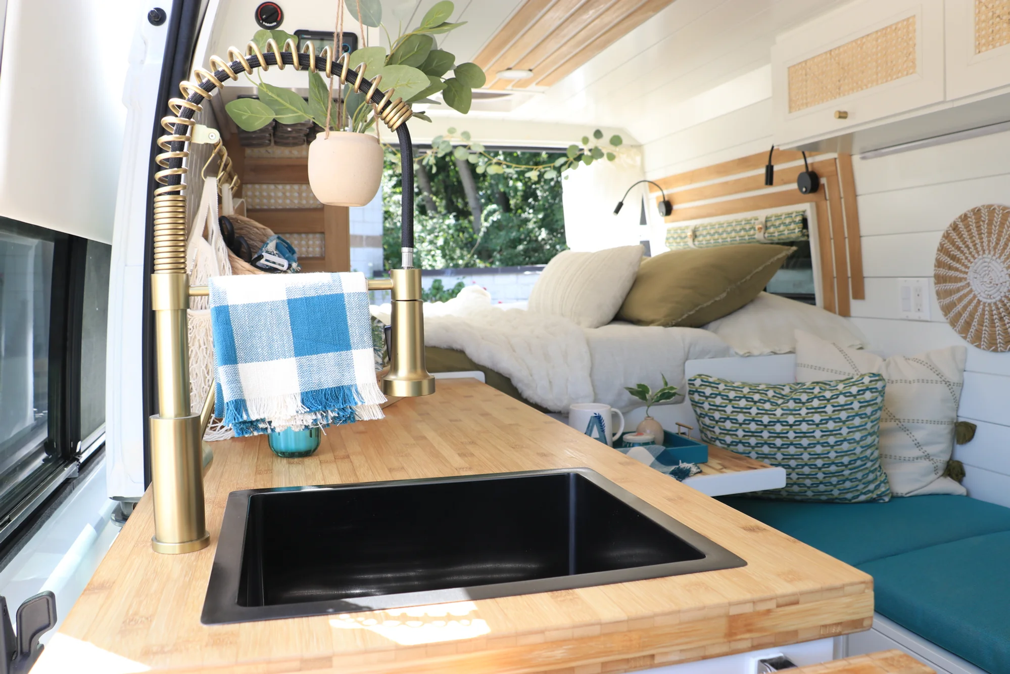 The Drifter 101 custom Ford Transit campervan built for Amy by Drifter Vans, with a natural bamboo countertop, hex tile backsplash, gold fixtures, and white cabinetry with blue accents