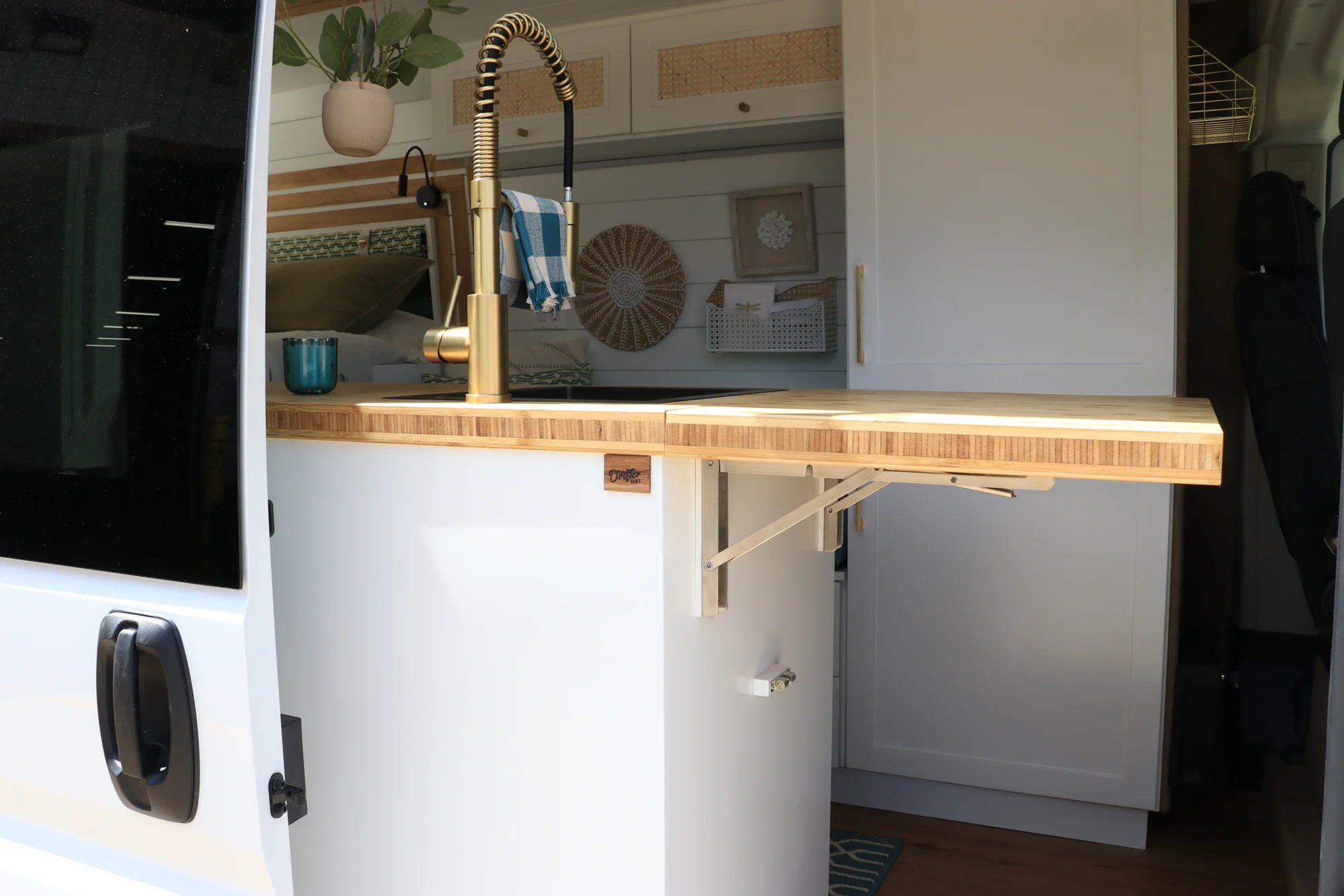 The Drifter 101 custom Ford Transit campervan built for Amy by Drifter Vans, with a natural bamboo countertop, hex tile backsplash, gold fixtures, and white cabinetry with blue accents