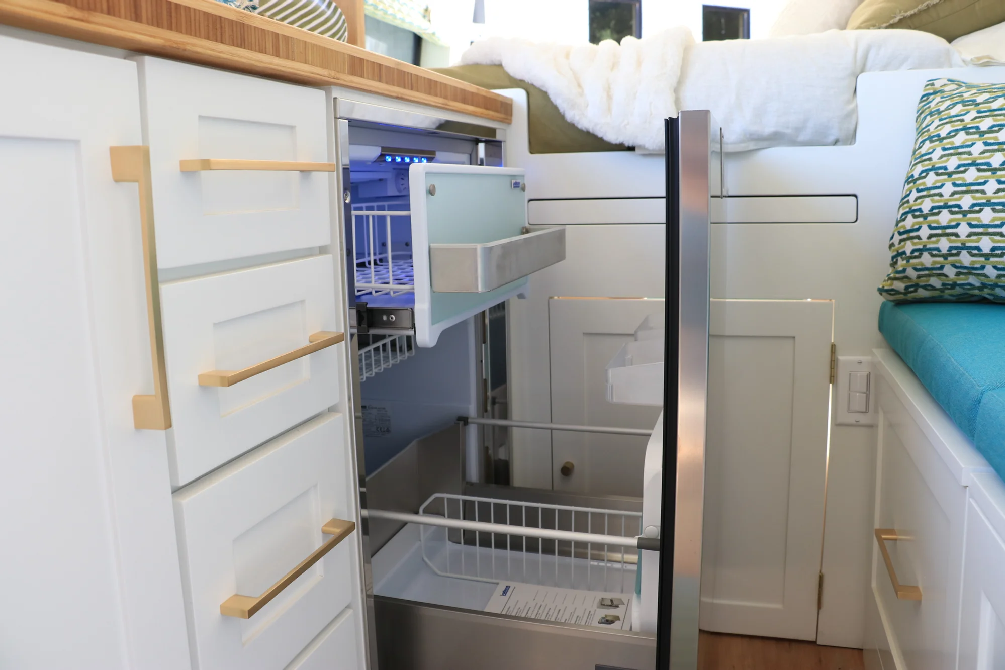 The Drifter 101 custom Ford Transit campervan built for Amy by Drifter Vans, with a natural bamboo countertop, hex tile backsplash, gold fixtures, and white cabinetry with blue accents