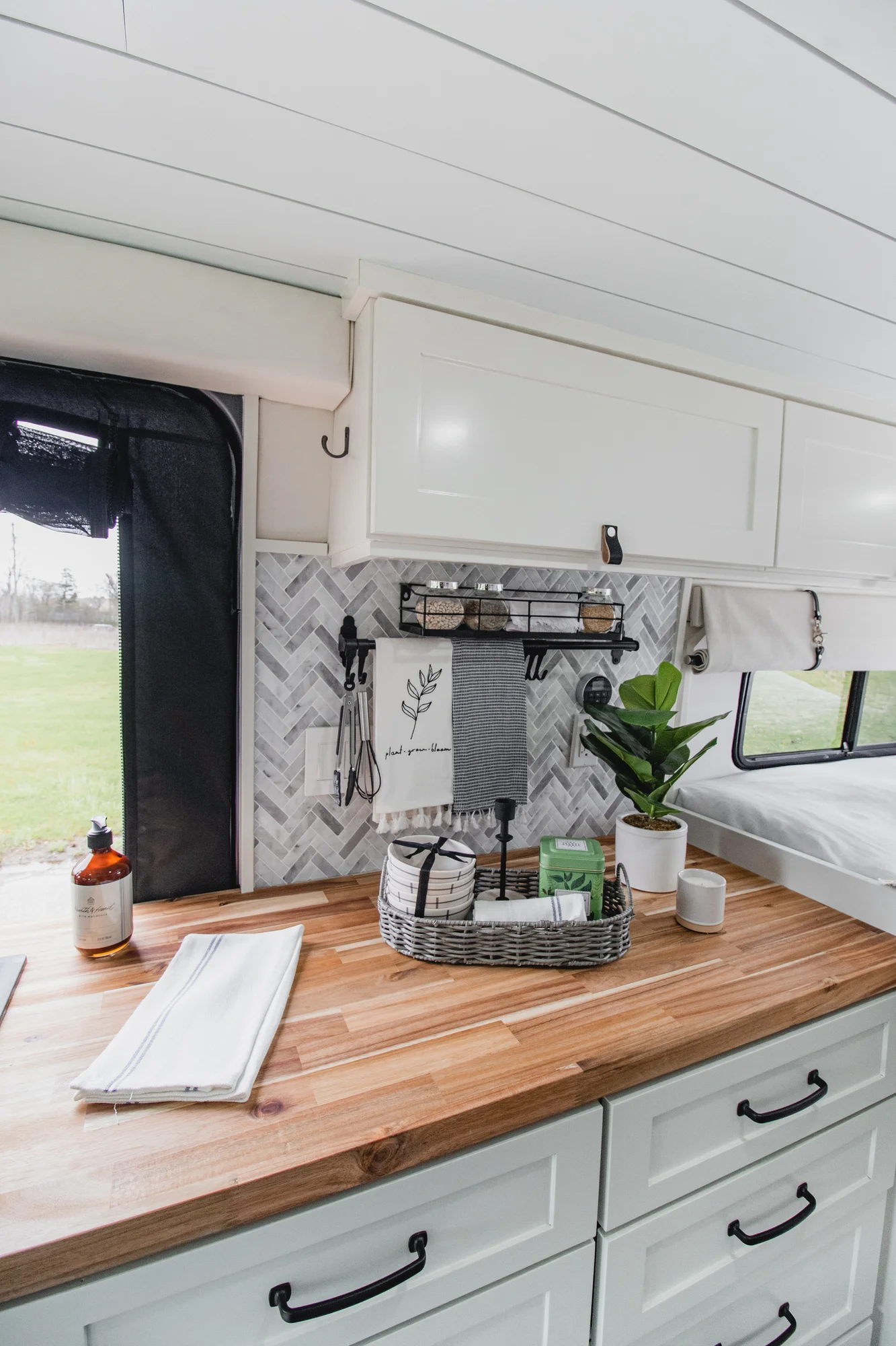 The Drifter 101 custom Ram ProMaster campervan built for Halley by Drifter Vans, Wanderer layout with a herringbone tile backsplash, butcher block countertop, and white cabinetry