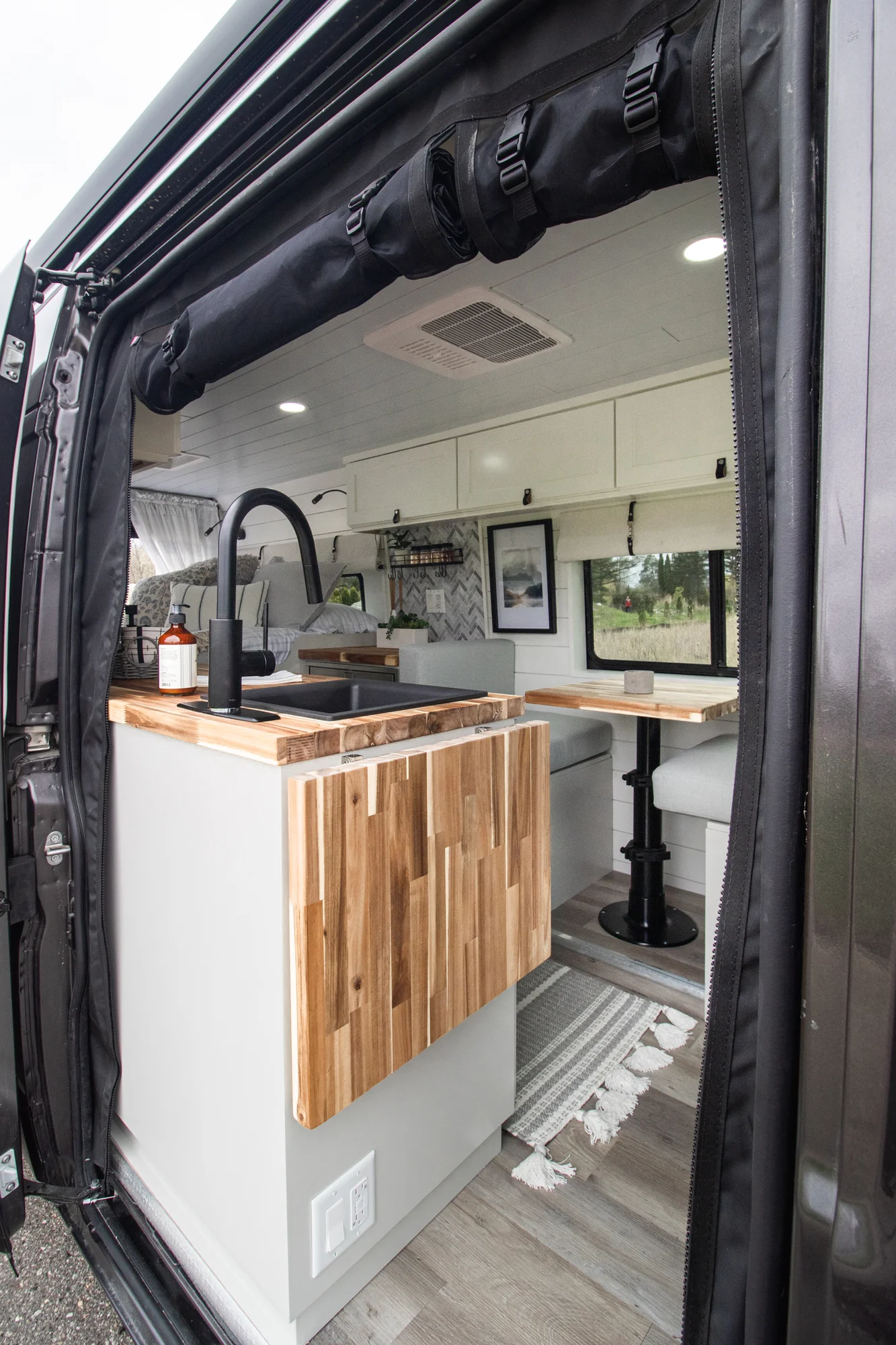 The Drifter 101 custom Ram ProMaster campervan built for Halley by Drifter Vans, Wanderer layout with a herringbone tile backsplash, butcher block countertop, and white cabinetry