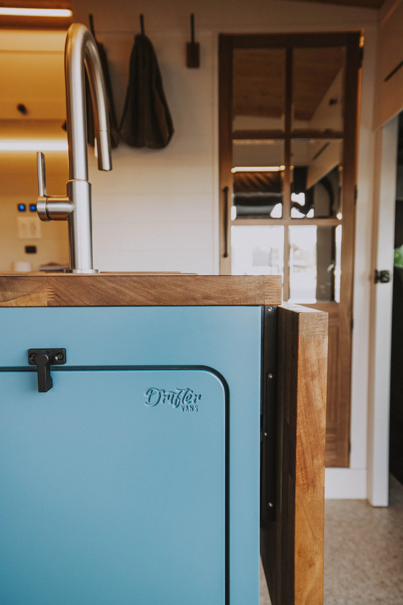 The Drifter 101 custom Ford Transit campervan built for Charlie and Linda by Drifter Vans, Nomadik layout with a Vermont slate shower, sky-blue cabinetry, and butcher block countertop