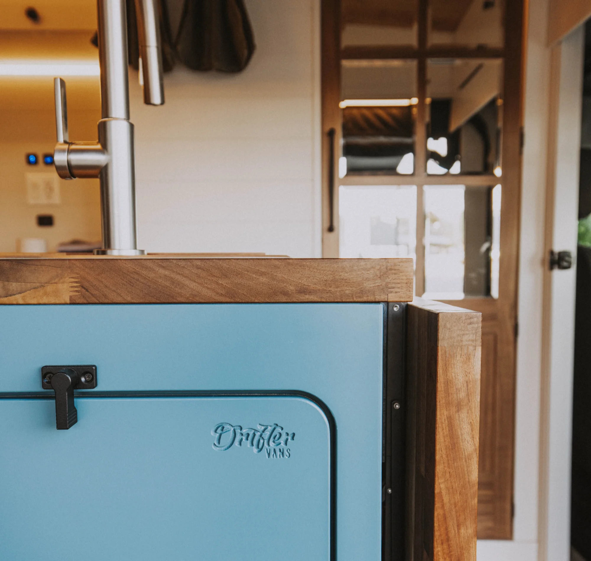 The Drifter 101 custom Ford Transit campervan built for Charlie and Linda by Drifter Vans, Nomadik layout with a Vermont slate shower, sky-blue cabinetry, and butcher block countertop