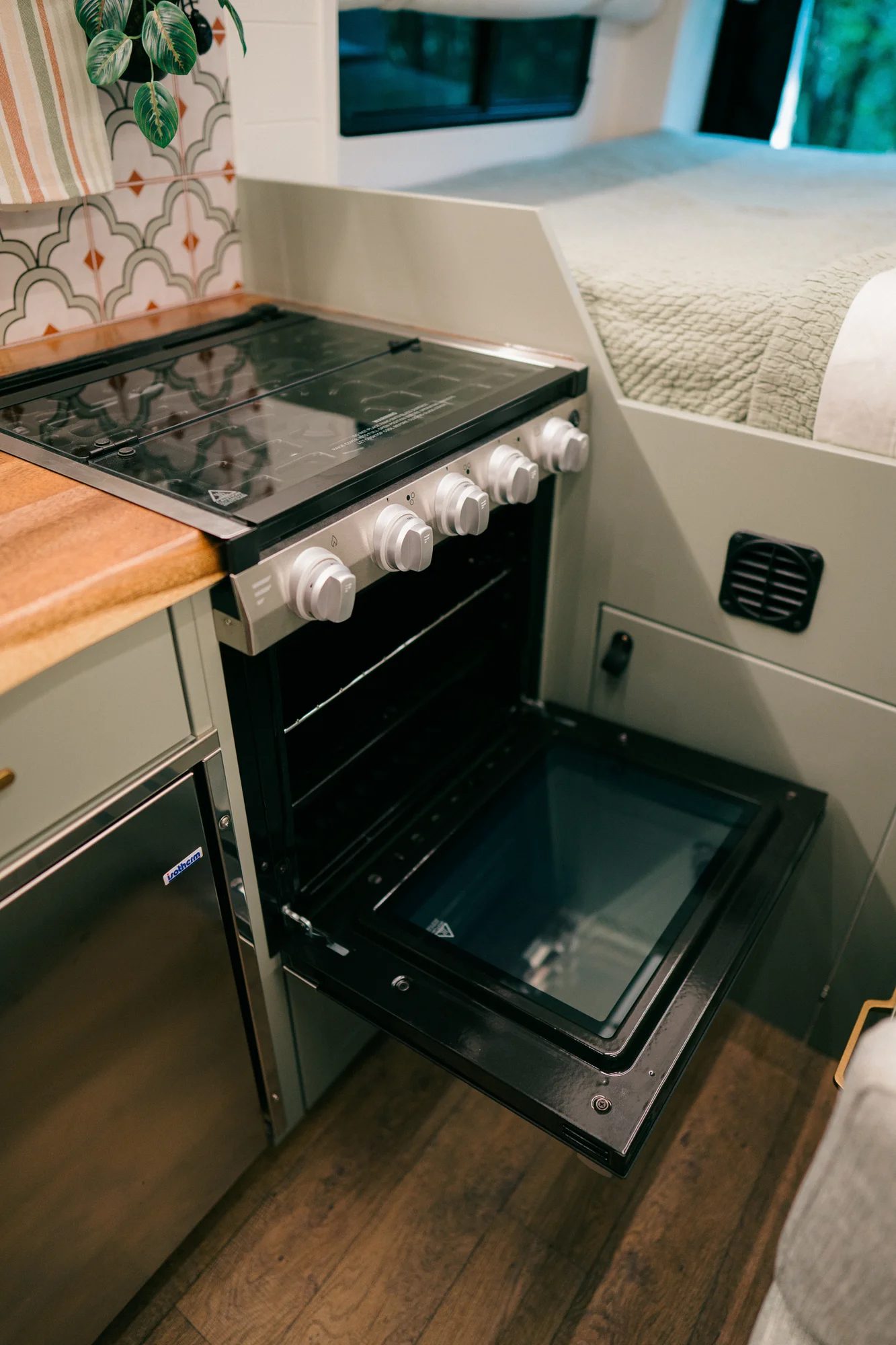 The Drifter 101 custom Ford Transit campervan built for Heather by Drifter Vans, Drifter layout with a full oven, patterned tile backsplash, brass faucet, and natural wood cabinetry