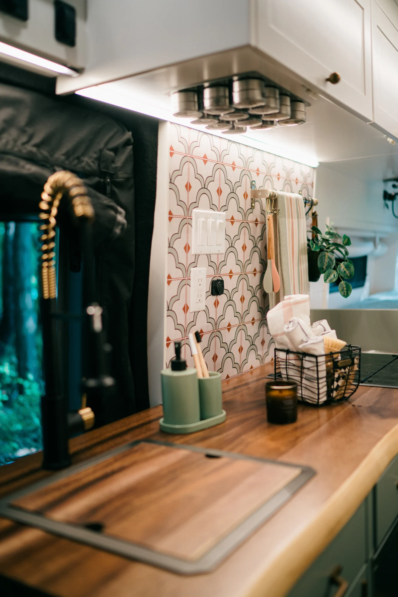 The Drifter 101 custom Ford Transit campervan built for Heather by Drifter Vans, Drifter layout with a full oven, patterned tile backsplash, brass faucet, and natural wood cabinetry
