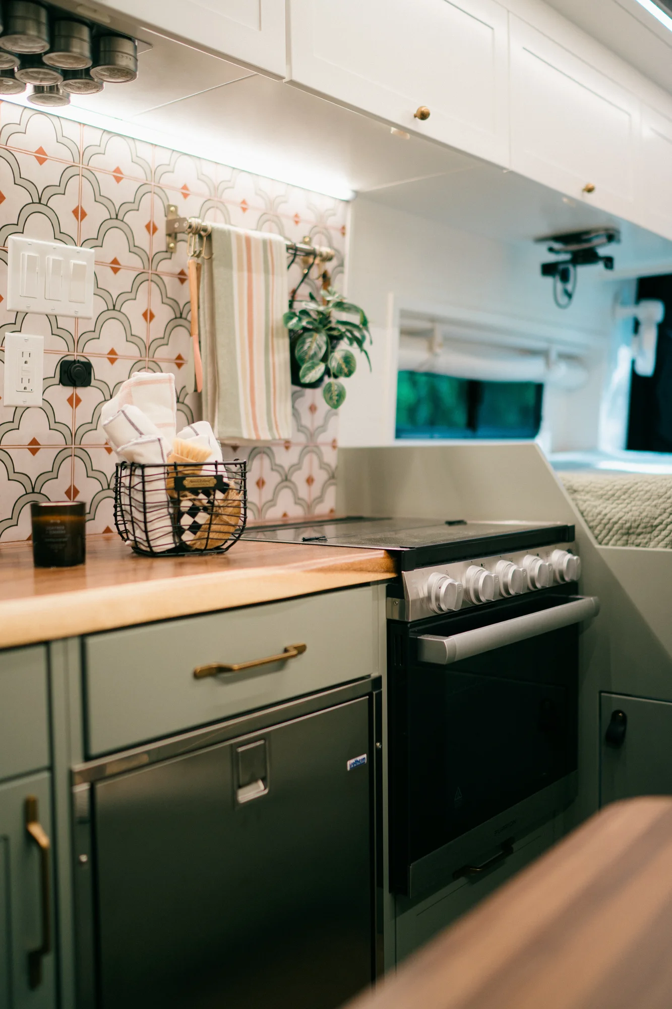 The Drifter 101 custom Ford Transit campervan built for Heather by Drifter Vans, Drifter layout with a full oven, patterned tile backsplash, brass faucet, and natural wood cabinetry