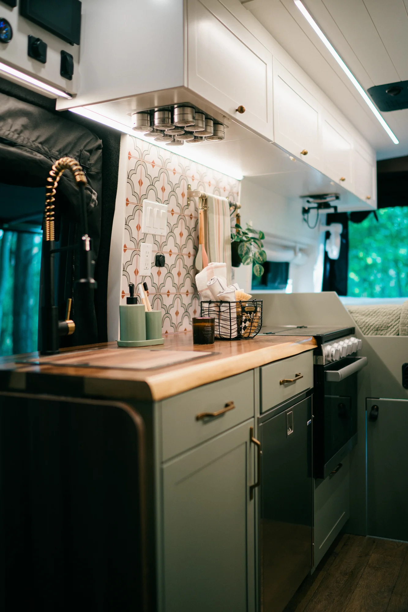 The Drifter 101 custom Ford Transit campervan built for Heather by Drifter Vans, Drifter layout with a full oven, patterned tile backsplash, brass faucet, and natural wood cabinetry