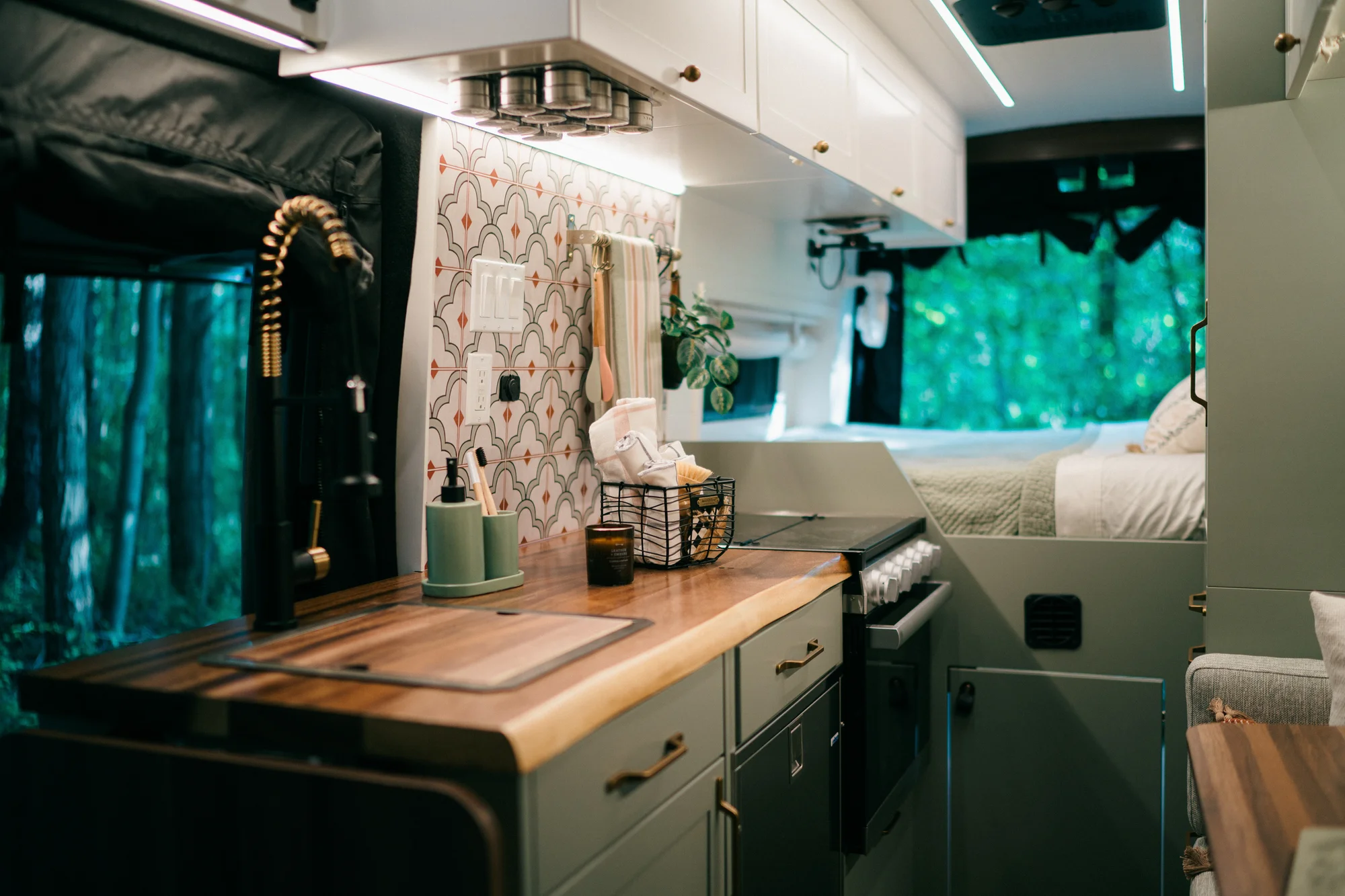 The Drifter 101 custom Ford Transit campervan built for Heather by Drifter Vans, Drifter layout with a full oven, patterned tile backsplash, brass faucet, and natural wood cabinetry