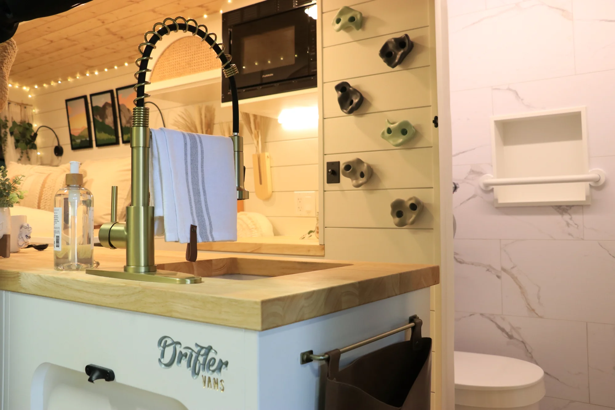 The Drifter 101 custom Ford Transit campervan built for Sarah by Drifter Vans, Nomadik layout with a marble-style wet bath, gold faucet, trifold privacy door, and boho accents