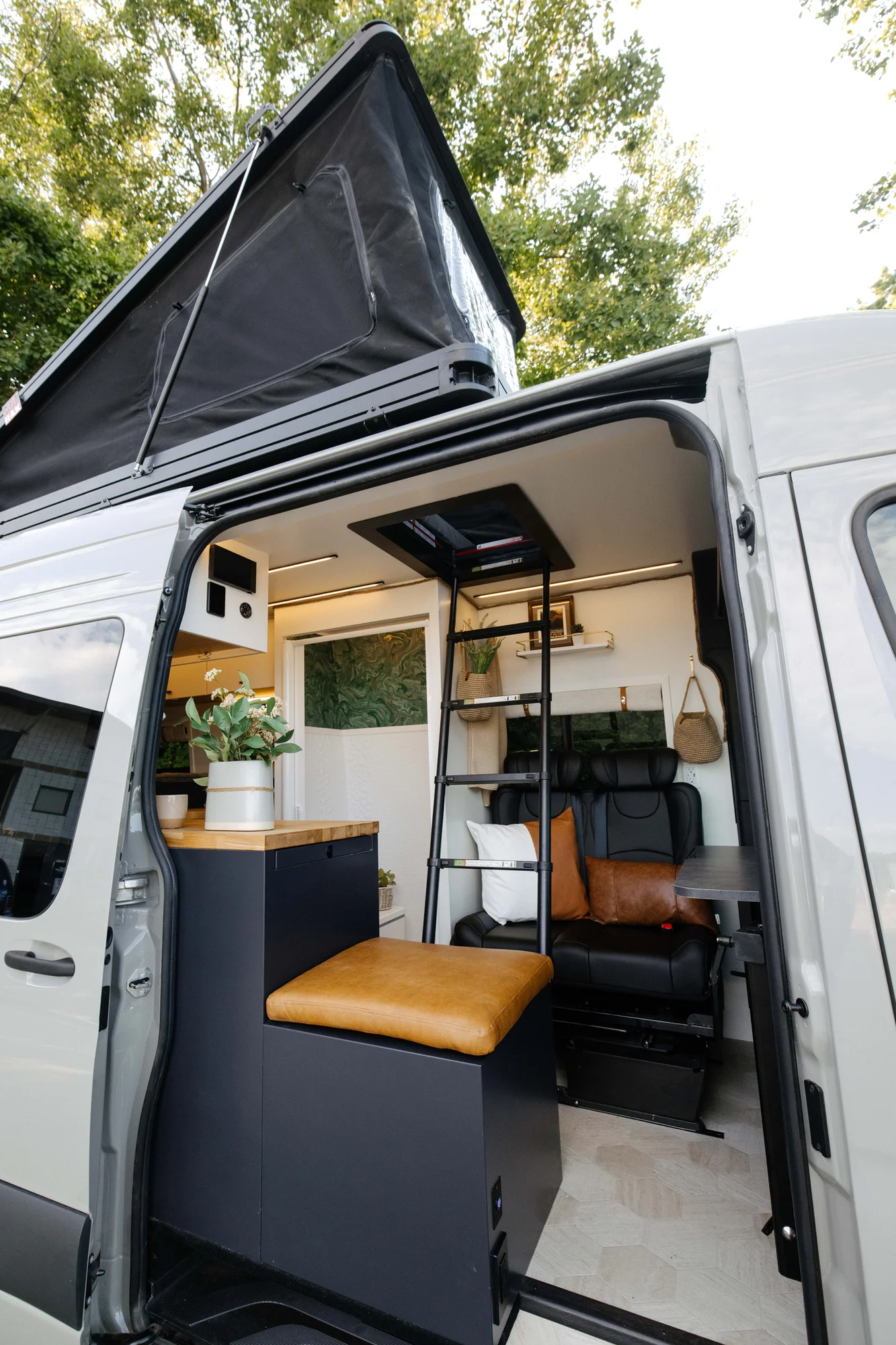The Drifter 101 custom Mercedes-Benz Sprinter campervan built for Amber by Drifter Vans, with a pop-top sleeping area, navy cabinetry, butcher block counters, and gold hardware