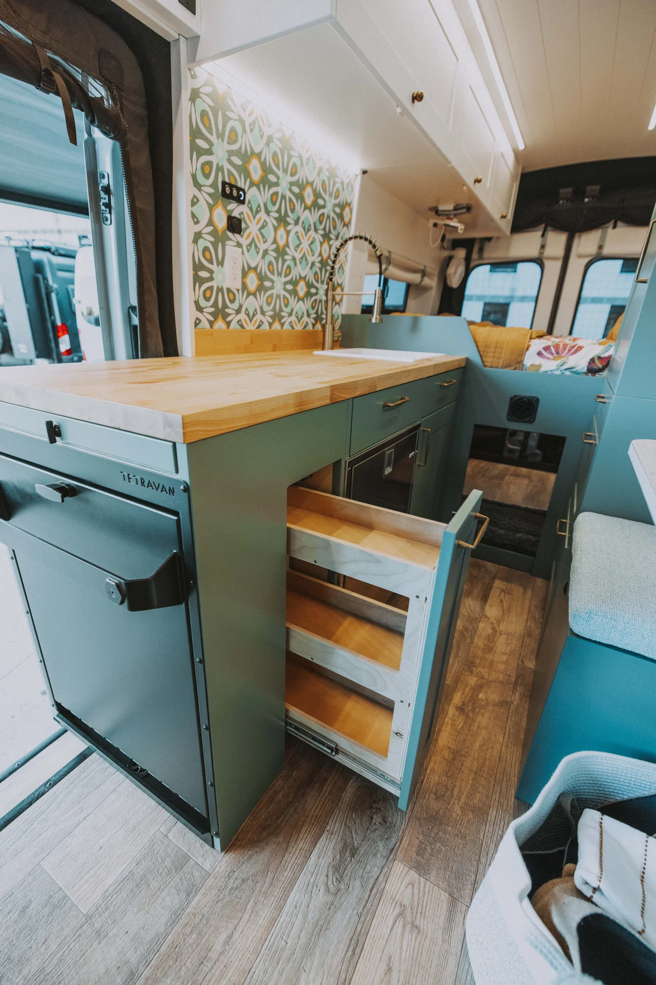 The Drifter 101 custom Ford Transit campervan built for Kristina by Drifter Vans, Drifter layout with a Moroccan-inspired blue tile backsplash, warm wood cabinetry, and a built-in dog nook