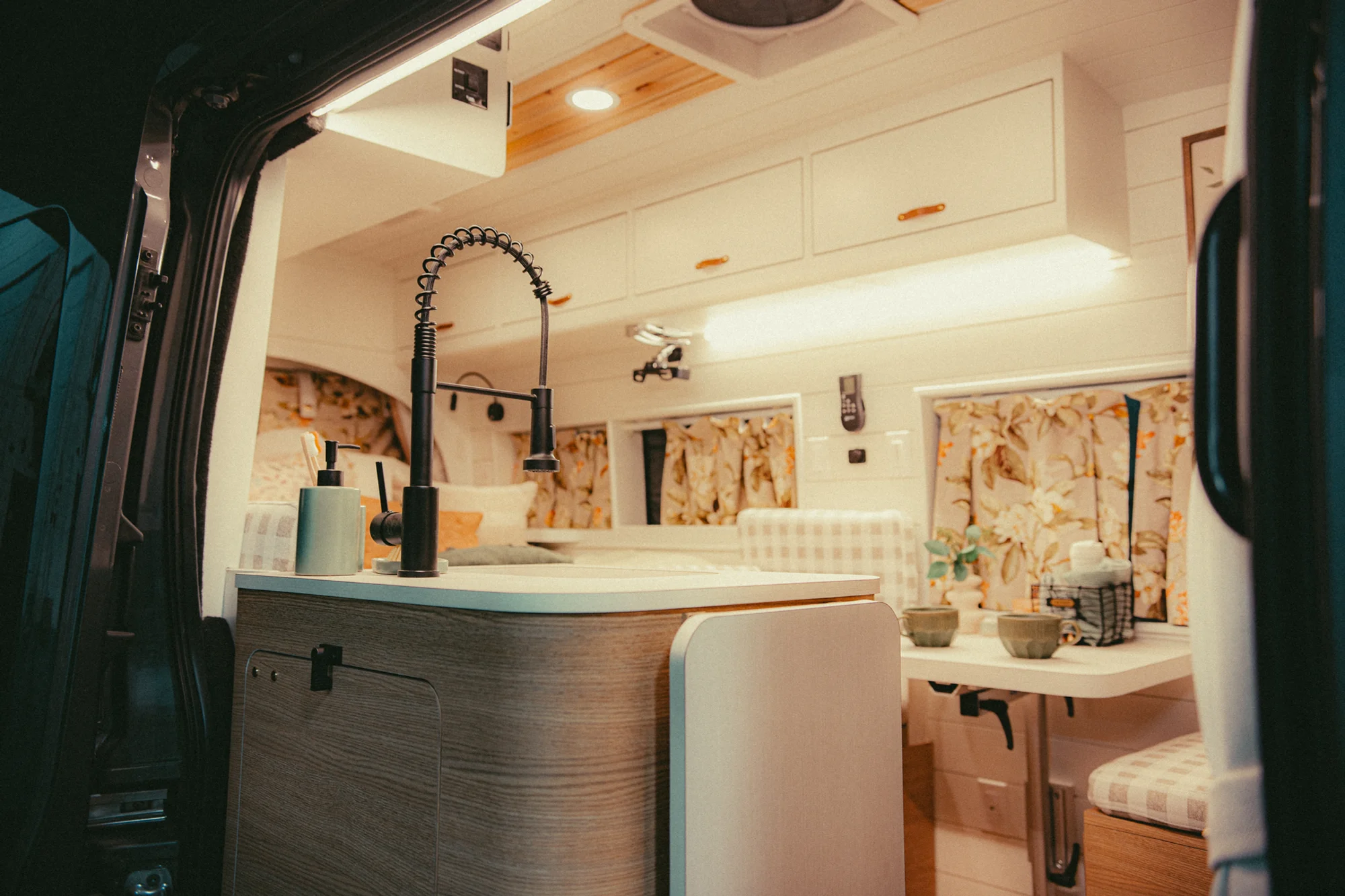 The Drifter 101 custom Ford Transit campervan built for Donna and Stanley by Drifter Vans, farmhouse interior with butcher block countertop, checkered cushions, and floral curtains